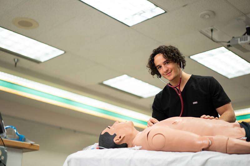 A GVSU transfer student practicing listening with a stethoscope